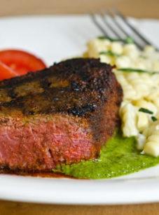 Grilled beef tenderloin filet with chimichurri on a plate with corn and tomatoes.