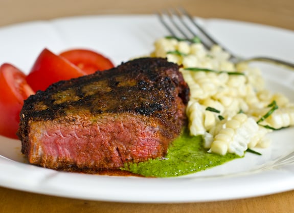 Grilled beef tenderloin filet with chimichurri on a plate with corn and tomatoes.