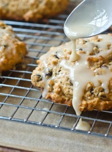 Spoon pouring glaze over oatmeal maple scones with pecans and currants.