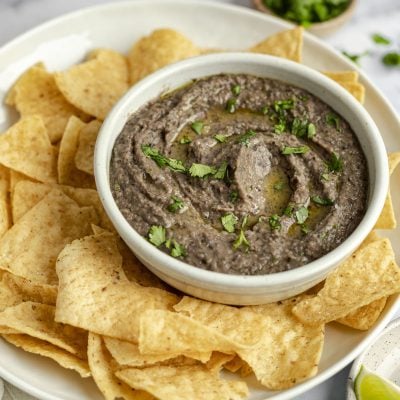 bowl of black bean dip on platter with tortilla chips.
