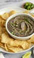bowl of black bean dip on platter with tortilla chips.