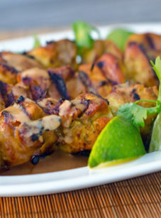Plate of grilled Thai curry chicken skewers with coconut-peanut sauce.