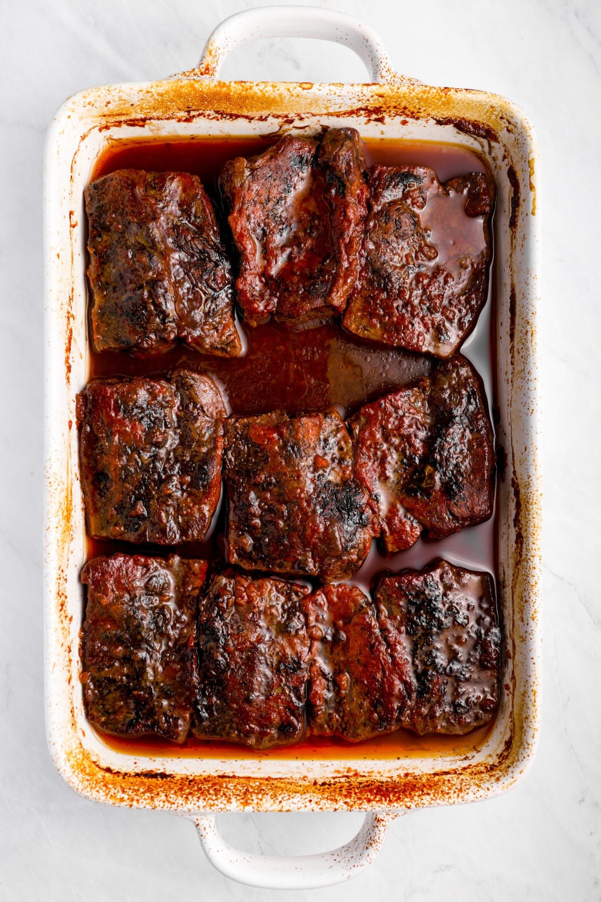 Short ribs in a pan of barbeque sauce.