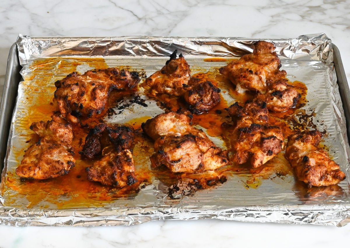 Barbeque-spiced chicken thighs on a lined baking sheet.