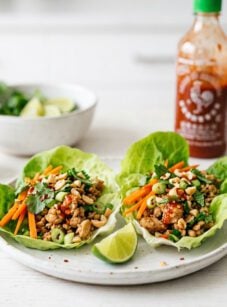 Thai chicken lettuce wraps on white plate with Sriracha bottle
