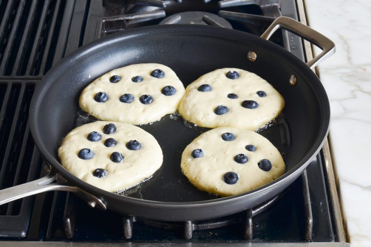 Blueberry pancakes cooking on a stovetop.