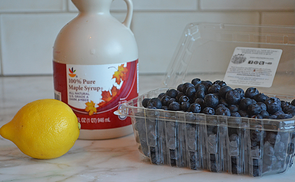 Lemon, blueberries, and maple syrup on a counter.