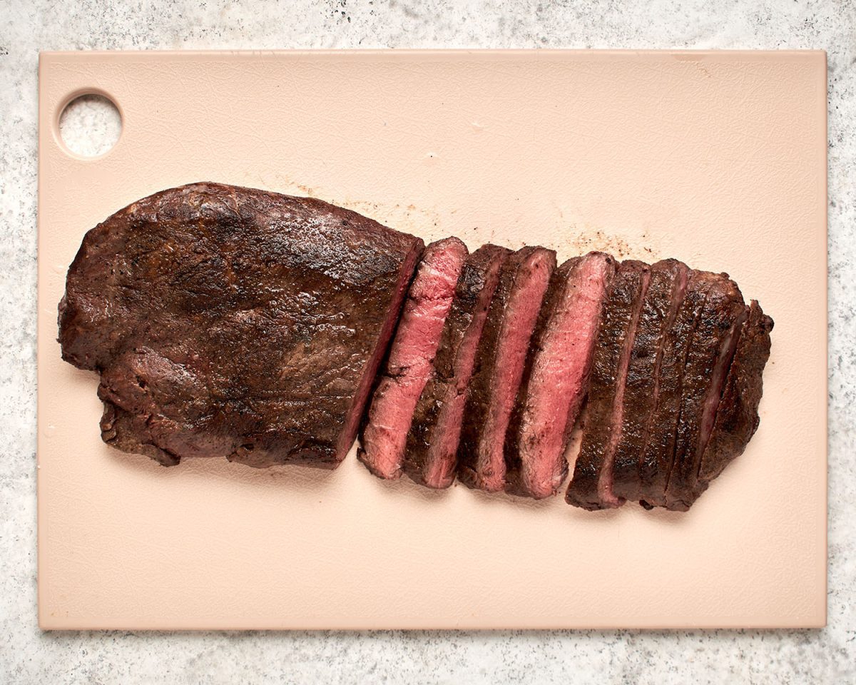 slicing the broiled flat iron steak on cutting board.