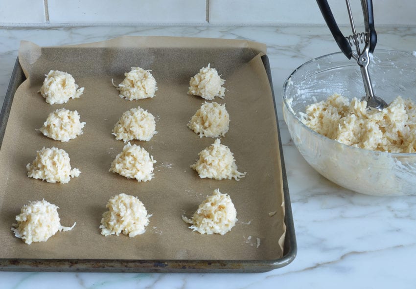 Scoops of coconut mixture on a lined baking sheet.