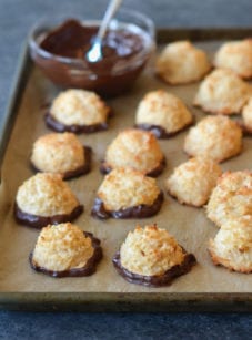 Coconut macaroons dipped in chocolate on a lined baking sheet.