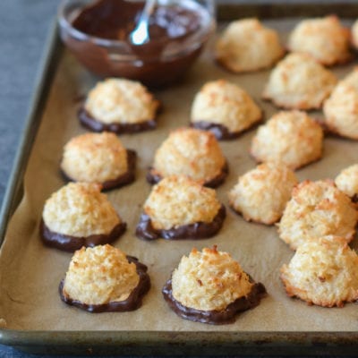 Coconut macaroons dipped in chocolate on a lined baking sheet.