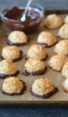 coconut macaroons on baking sheet with bowl of dipping chocolate.