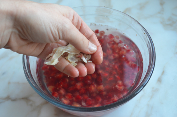 Person removing a membrane from a bowl of water and pomegranate arils.