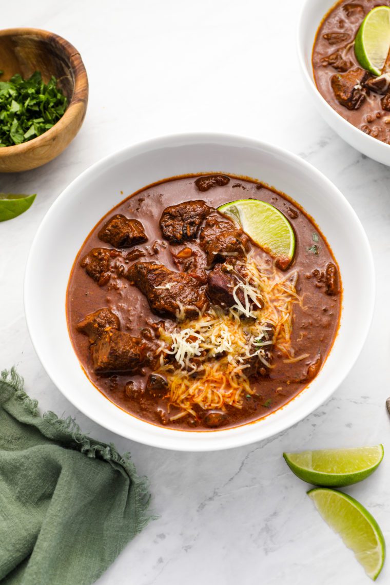 chili con carne in bowls with shredded cheese and limes
