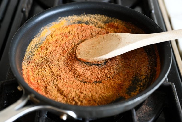 Wooden spoon stirring toasting spices in a pan.