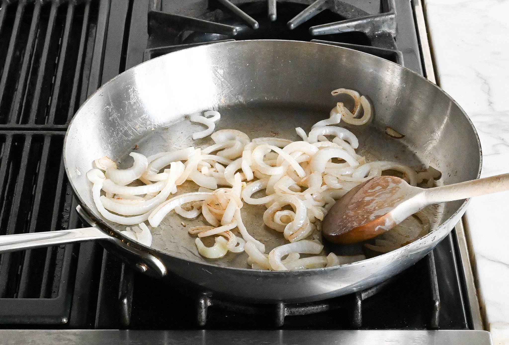 Stir-frying thinly sliced onions in a skillet with a wooden spoon.