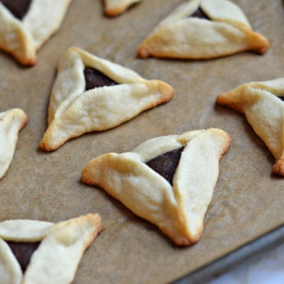 Chocolate-filled hamantaschen on a lined baking sheet.