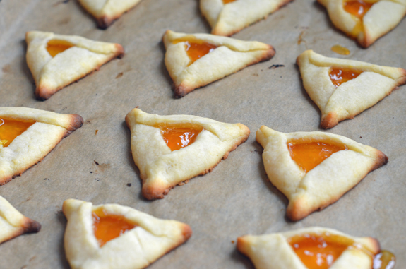 Baked apricot hamantaschen on a lined baking sheet.