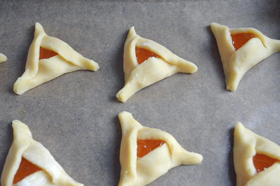 Unbaked apricot hamantaschen on a lined baking sheet.