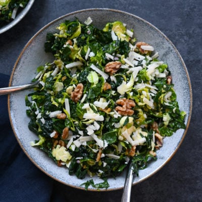 Forks on a plate of kale and brussels sprout salad with walnuts, parmesan, and lemon-mustard dressing.
