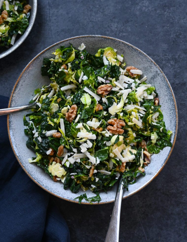 Forks on a plate of kale and brussels sprout salad with walnuts, parmesan, and lemon-mustard dressing.