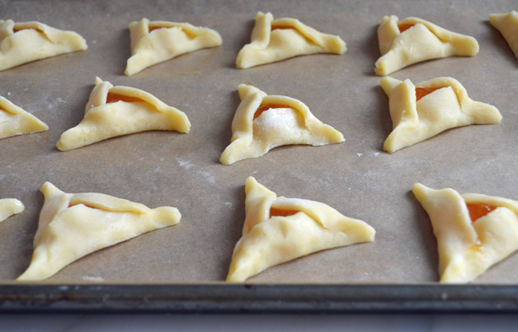 Unbaked apricot hamantaschen on a lined baking sheet.