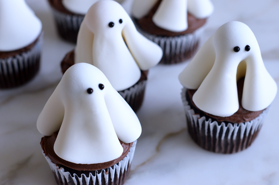Cupcakes decorated with lollipop and fondant ghosts with eyes.