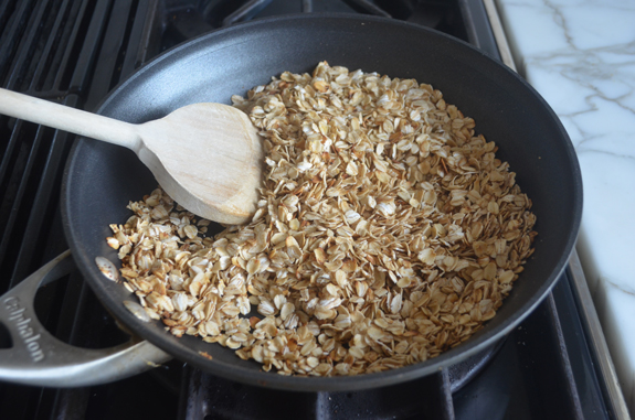 Wooden spoon stirring oats toasting in a skillet.