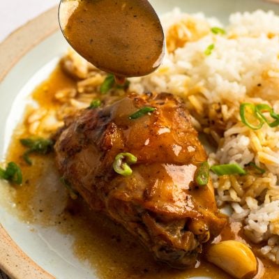 Spoon drizzling sauce over a plate of chicken and rice.