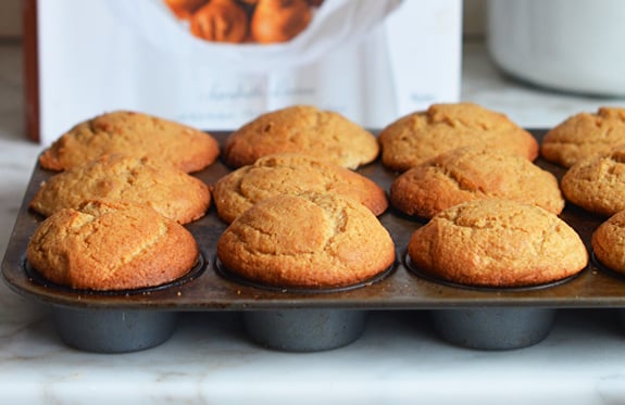 Muffin tin of maple muffins in front of a cookbook.