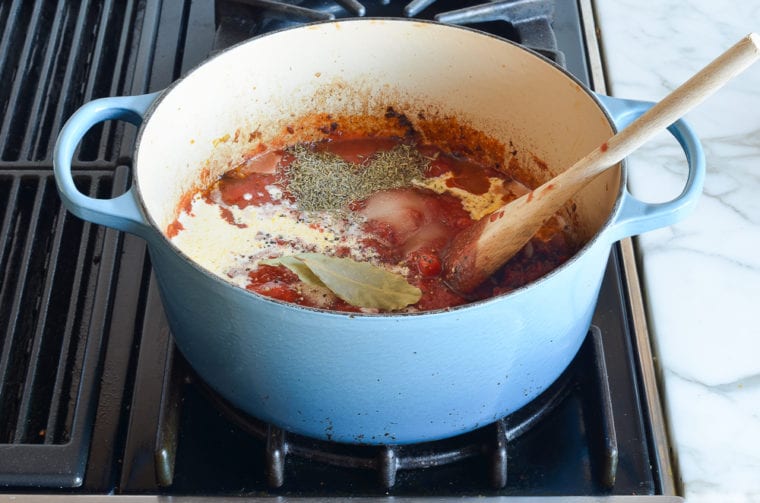 adding crushed tomatoes, cream, and seasoning to pot
