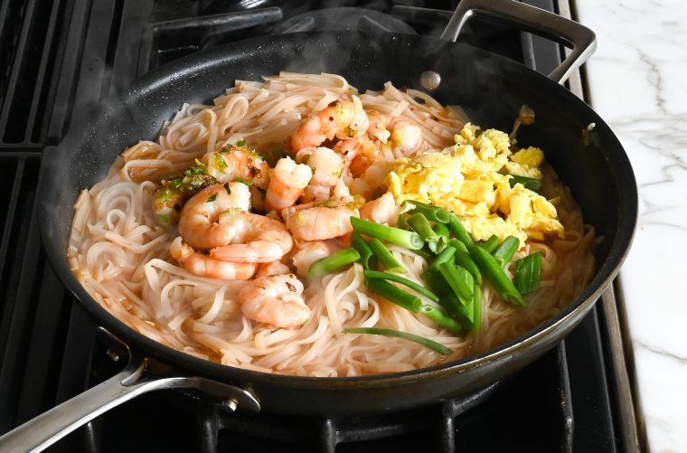 adding the shrimp, eggs, and scallions to the noodles