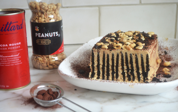 Chocolate peanut butter icebox cake topped with cocoa powder, crushed wafers, and peanuts.