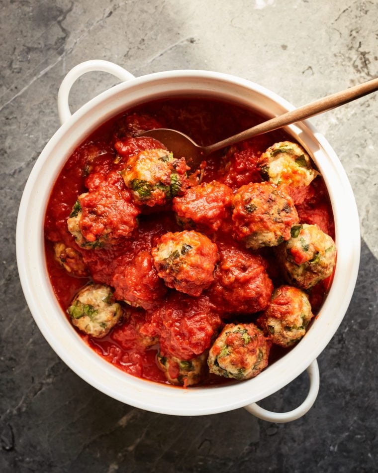 Spoon grabbing a meatball from a dish.