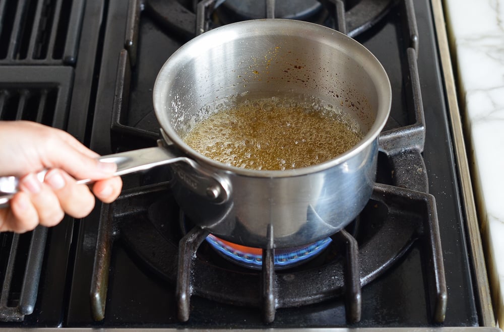 Sugar and water mixture turning honey color in a saucepan.