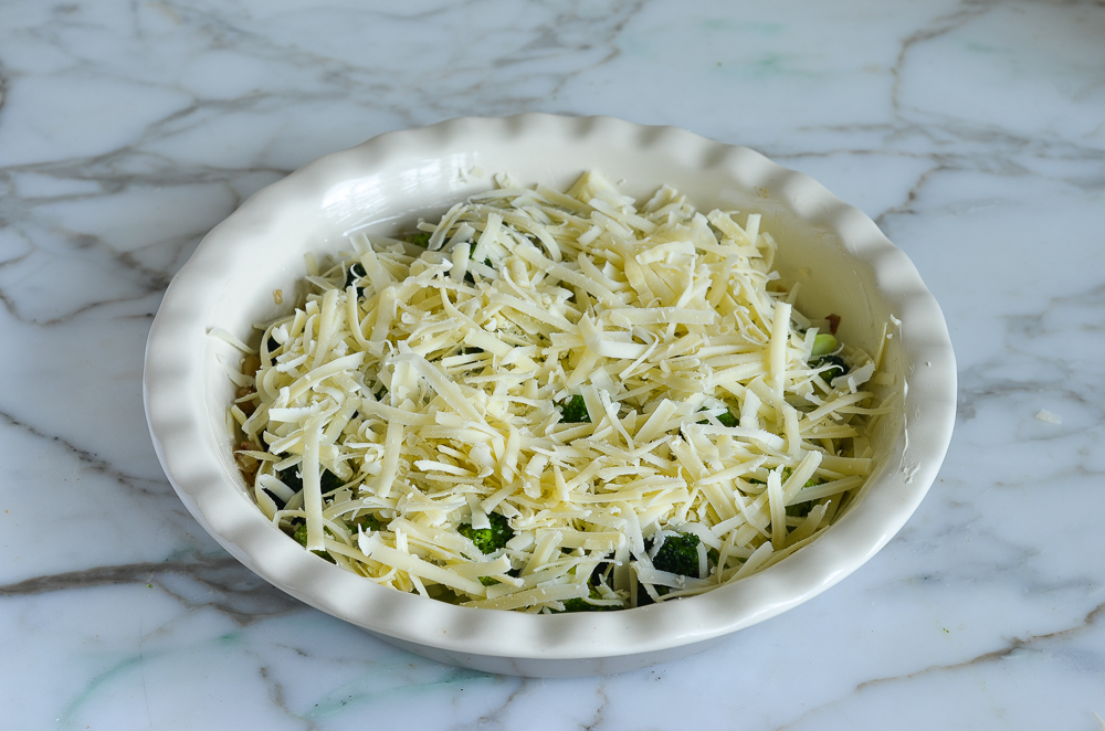 Shredded cheese in a pie pan with broccoli.