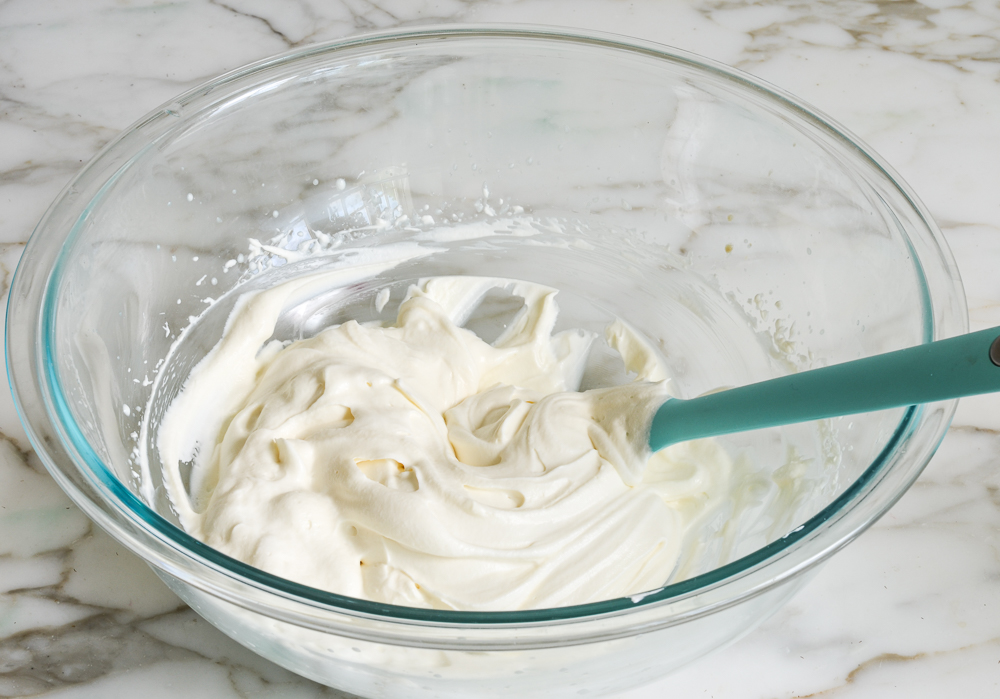 Spatula folding yogurt into whipped cream.