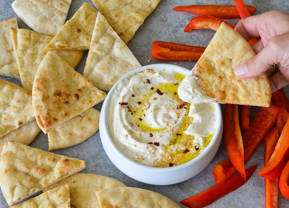 Person dipping toasted pita into creamy whipped feta dip.