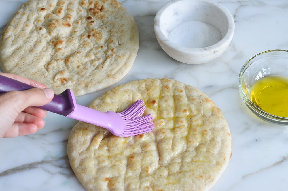 Person brushing pita bread with olive oil.