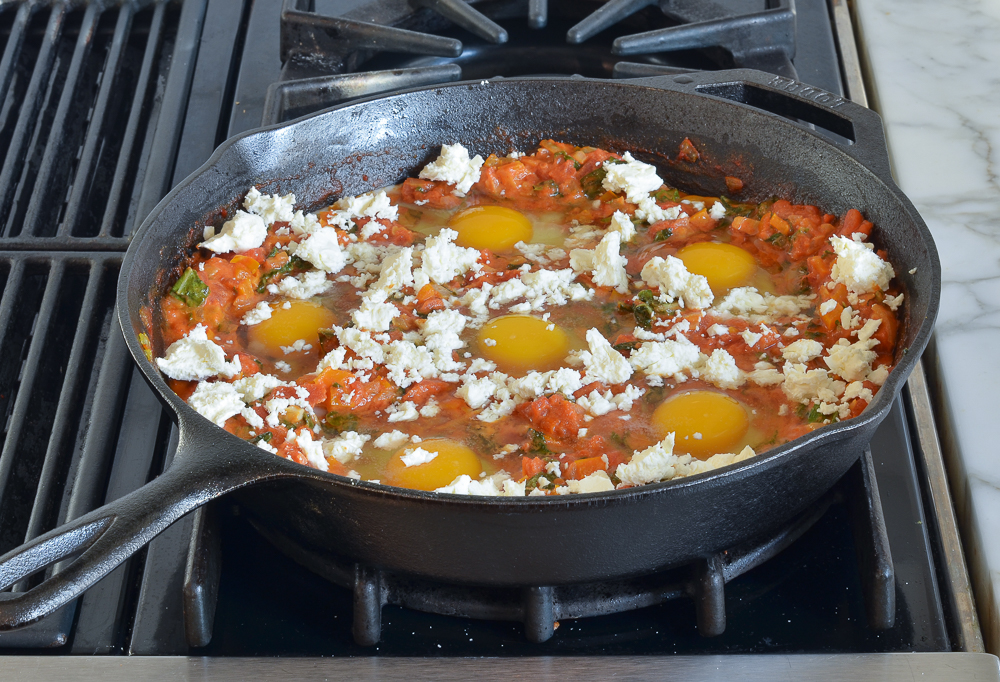 skillet with sauce, uncooked eggs and feta 