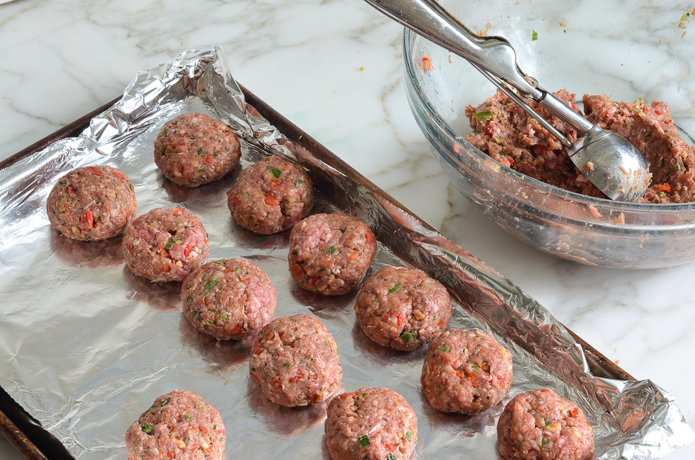 Balls of meat on a lined baking dish.