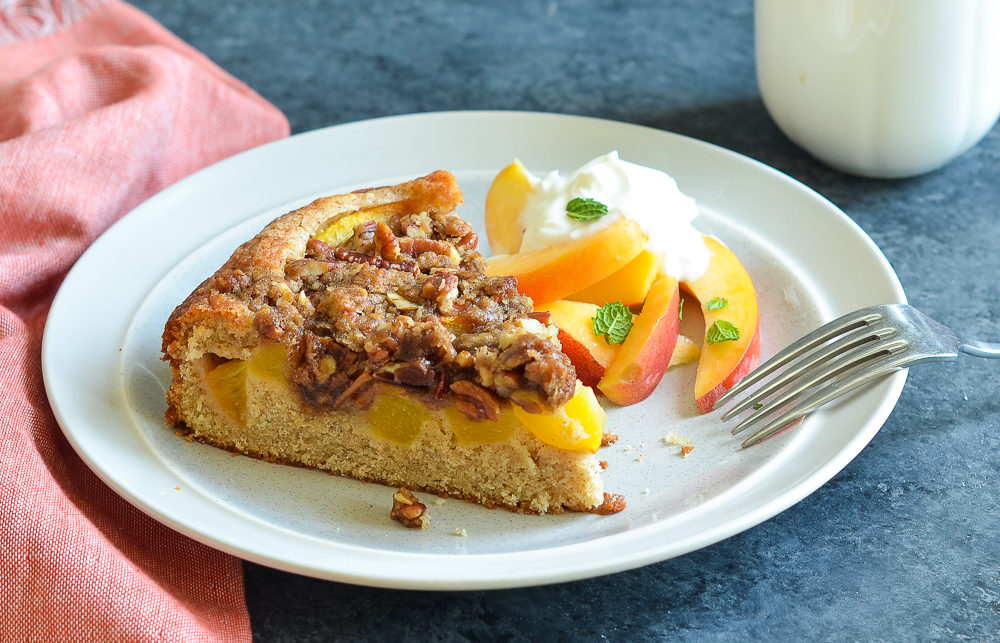 Slice of peach cake on a plate with peaches.