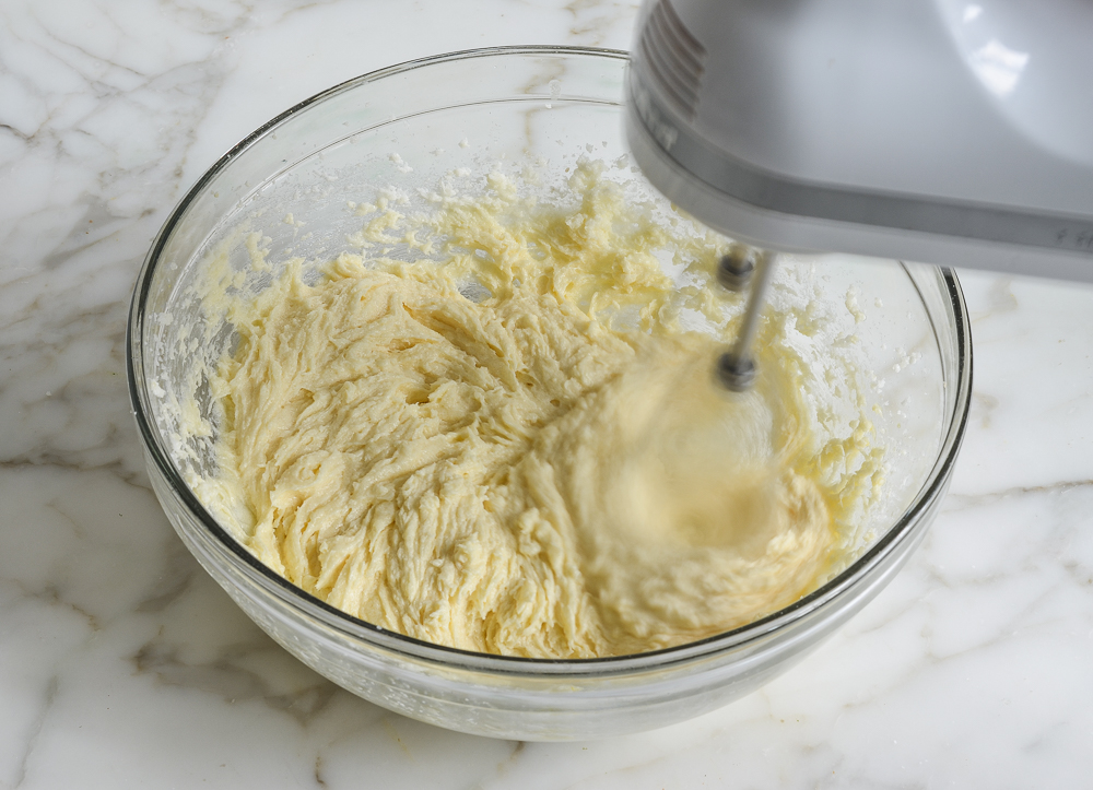 Electric mixer beating a bowl of butter mixture.