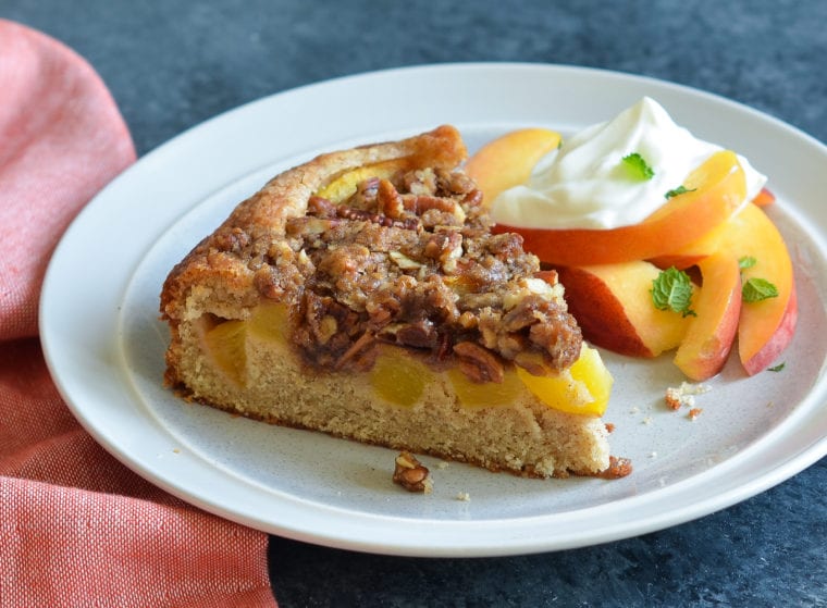 Slice of peach cake on a plate with peaches.