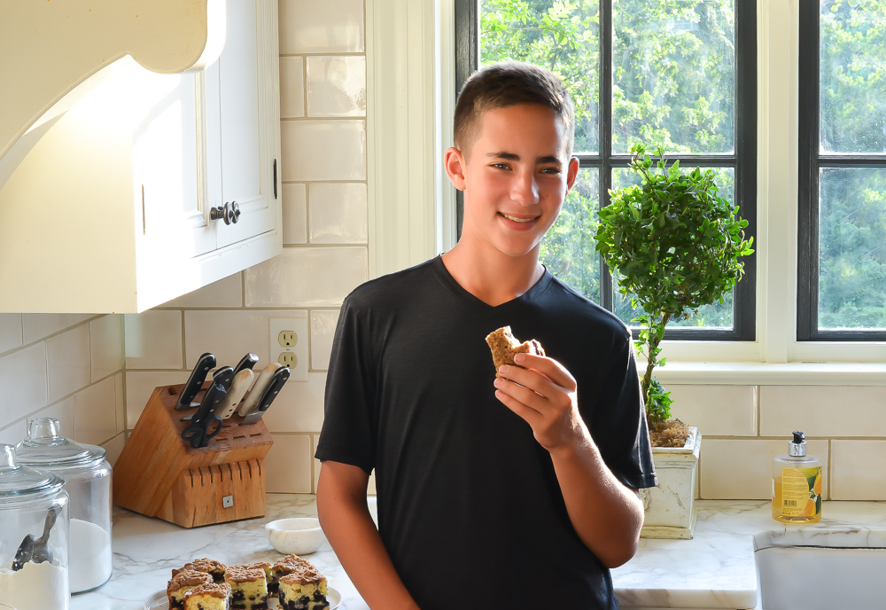 Boy holding a piece of blueberry coffee cake that is missing a bite.
