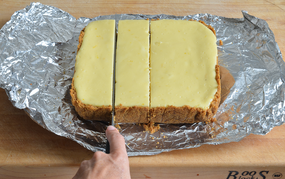 Person slicing baked cheesecake on aluminum foil.