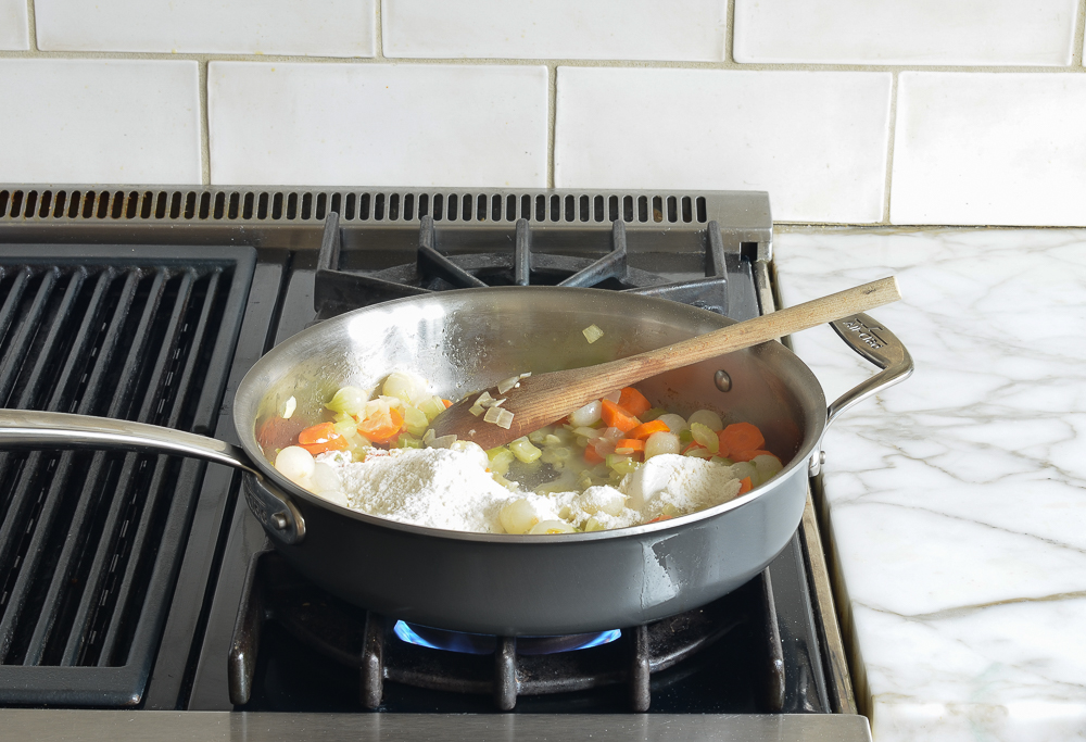 Flour in a skillet with cooked vegetables.