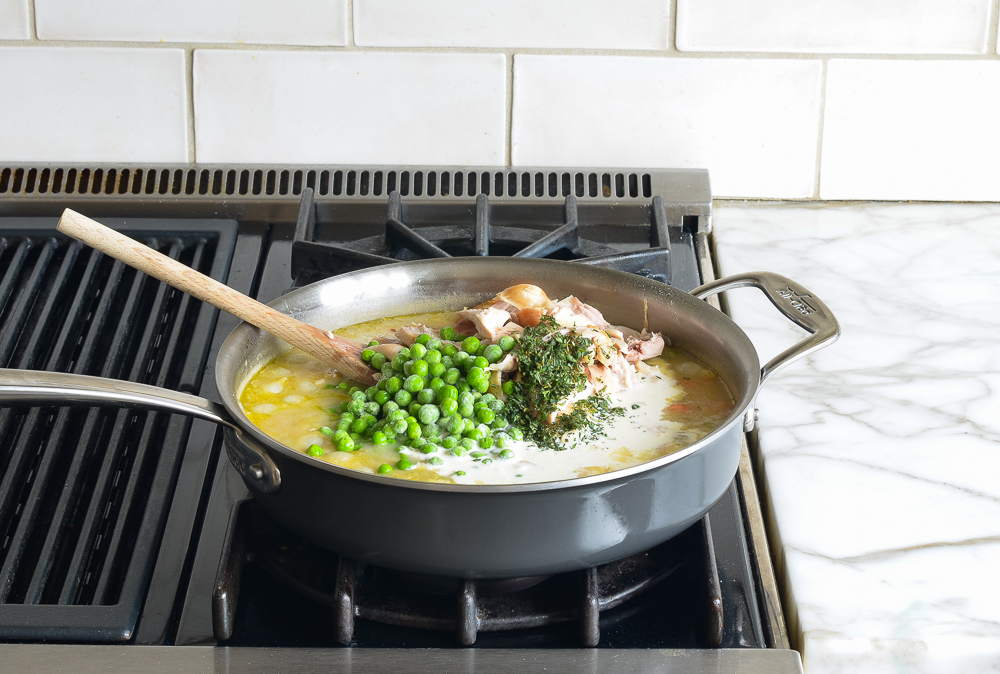 Peas, chicken, and seasonings added to a skillet of broth.