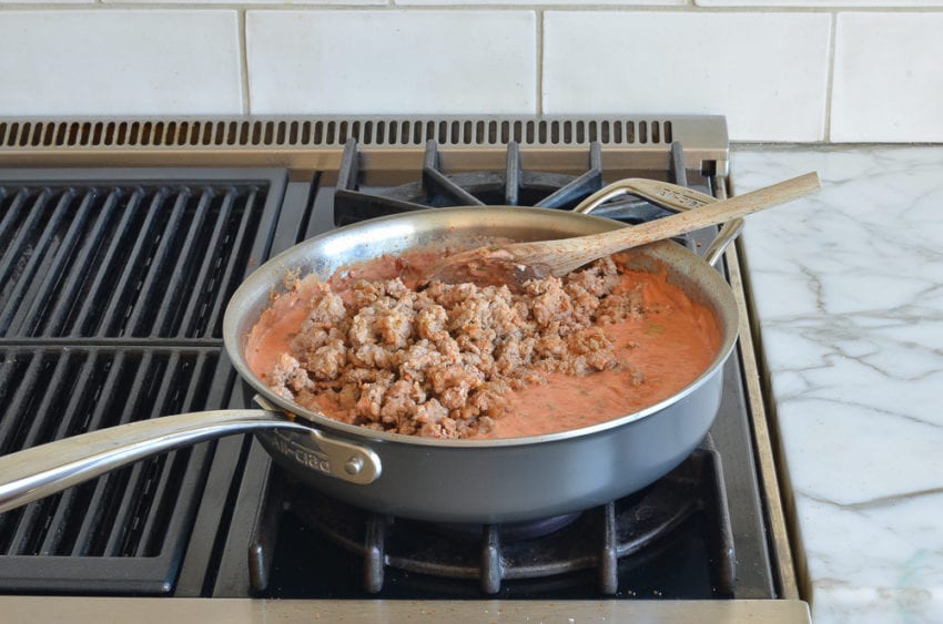 cooked sausage added to creamy tomato sauce in skillet
