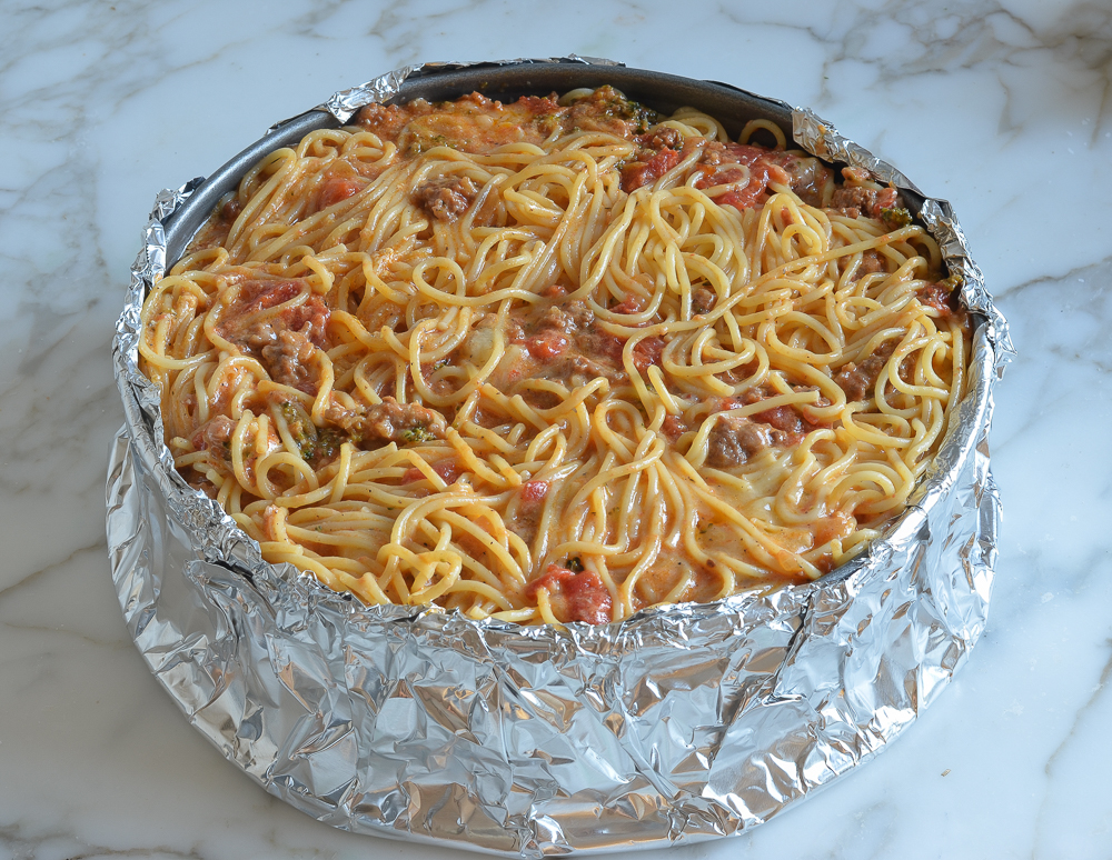 Pasta mixture in a springform pan wrapped in aluminum foil.
